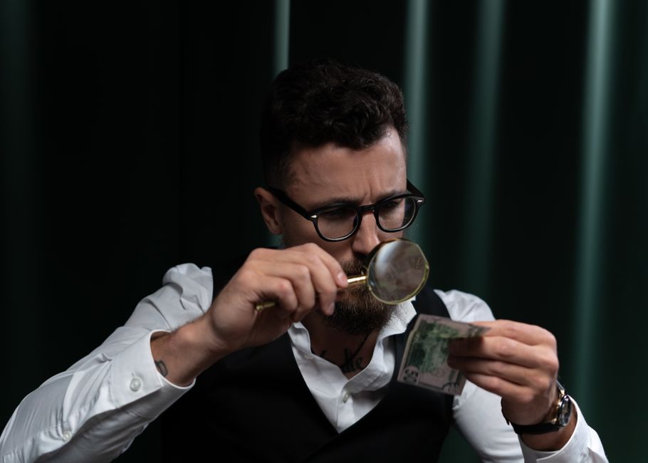 How to spot a Ponzi scheme, magnifying glass examining money for investment fraud red flags